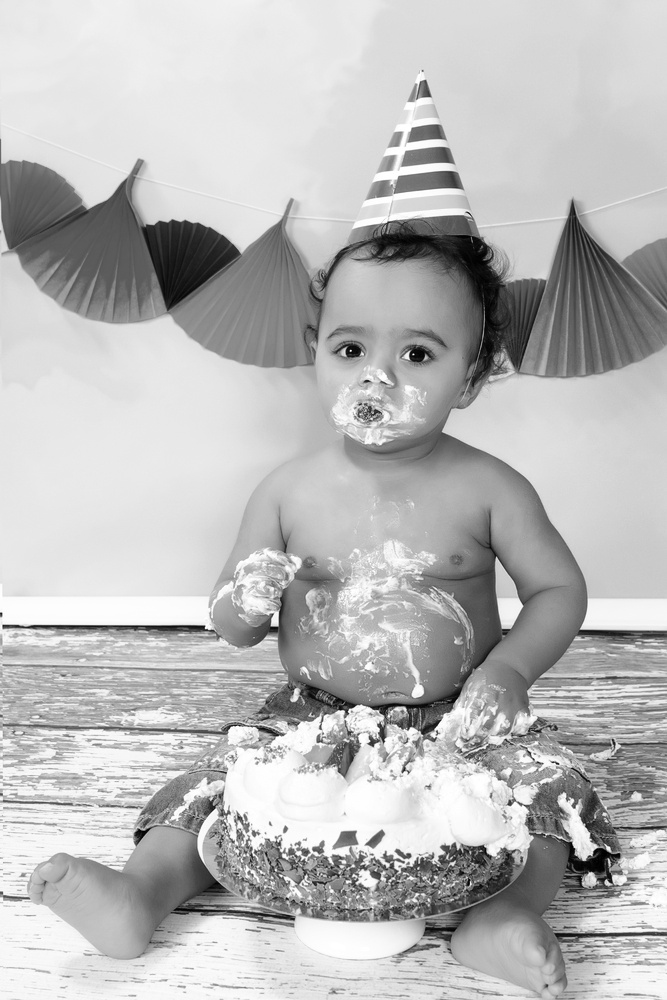 Baby eating cake, which is smeared all around the baby's mouth.